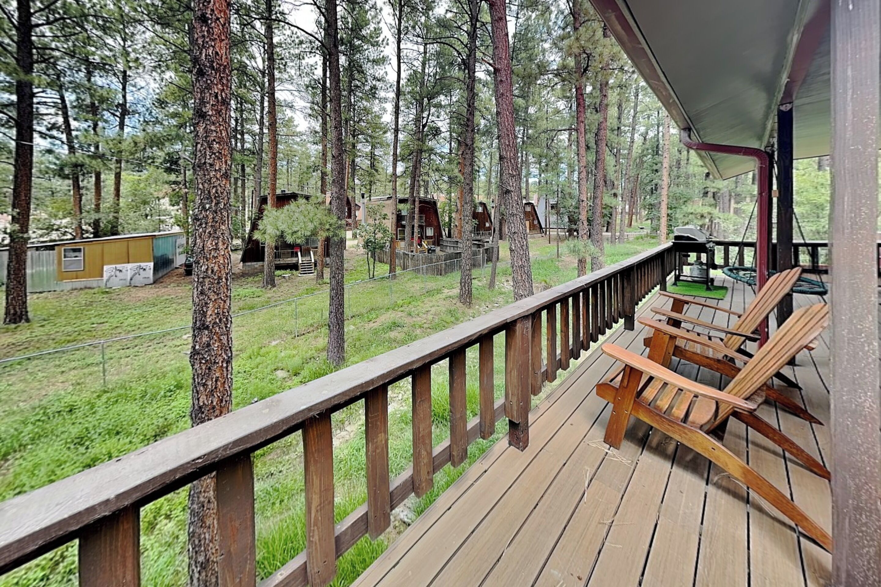 A wooden deck with outdoor seating, surrounded by tall trees.