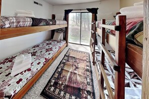 Ein schmales Zimmer mit Etagenbetten, einem Fenster mit Vorhängen und einem gemusterten Teppich.