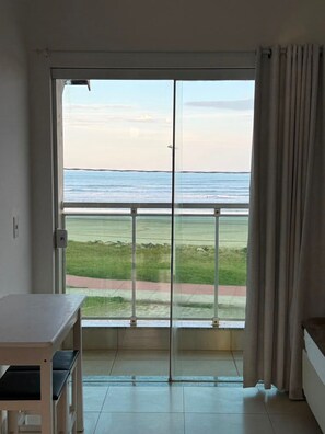 A room with a sliding glass door leading to a balcony with a view of the ocean.