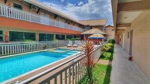 A hotel with a swimming pool, outdoor seating, and a covered area with a colorful umbrella.
