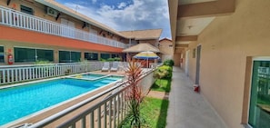 A hotel with a swimming pool, outdoor seating, and a covered area with a colorful umbrella.