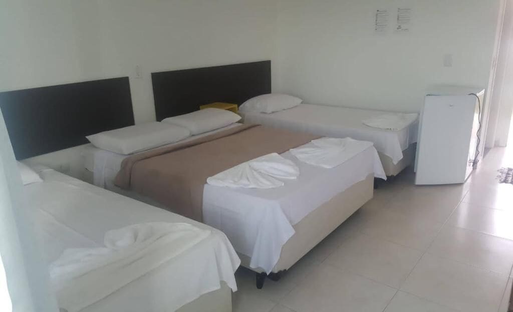Habitación de hotel con cama, mesita de noche, refrigerador y panel de control en la pared.