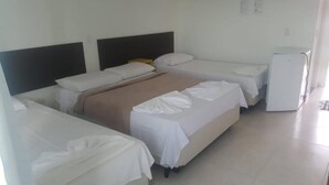 Quarto de hotel com cama, mesa de cabeceira, geladeira e painel de controle fixado na parede.
