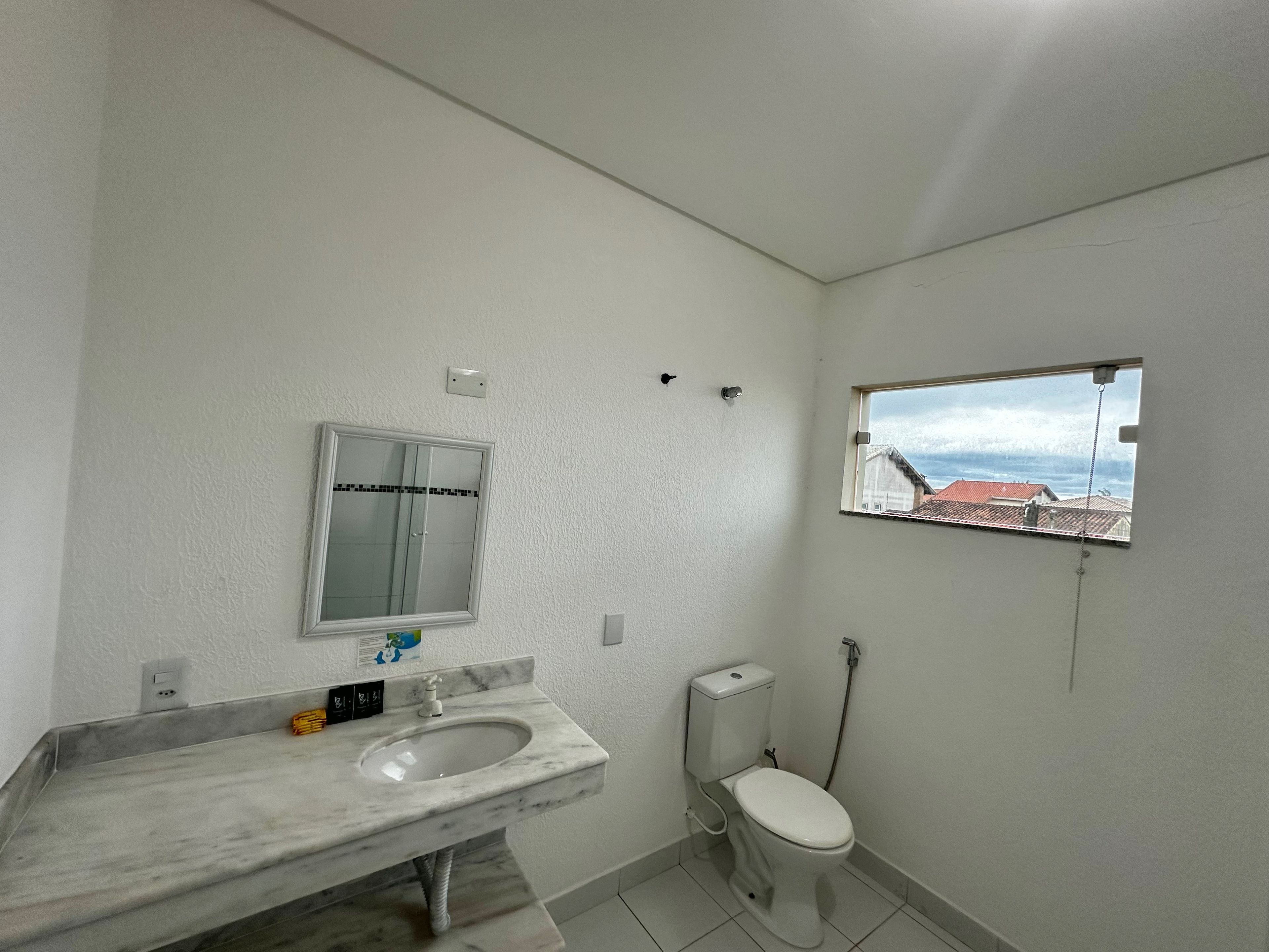 Een badkamer met een marmeren wastafel, toilet en een raam met uitzicht op gebouwen.
