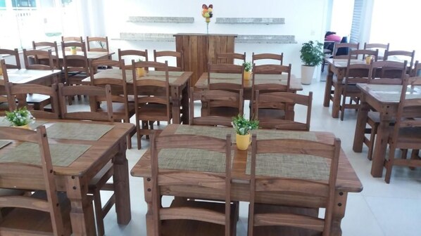 A dining area with multiple wooden tables and chairs, some with woven seat pads.