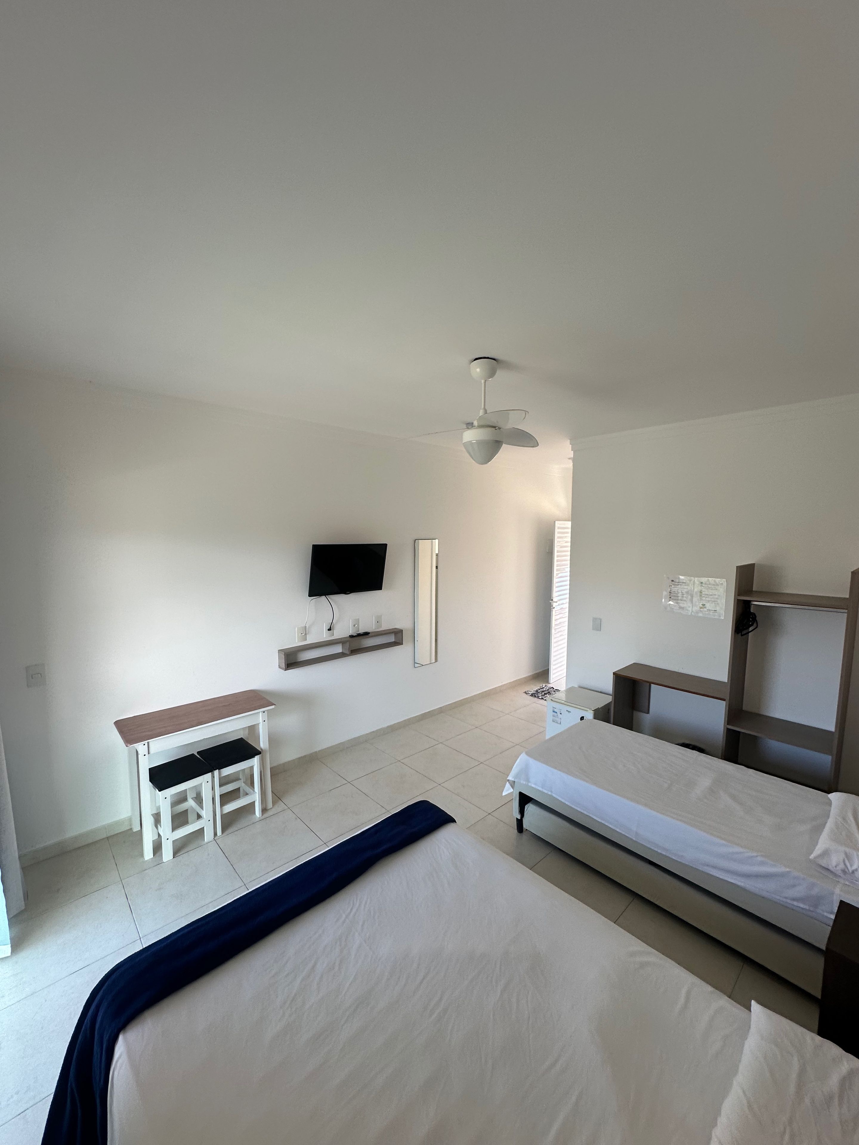 Een slaapkamer met een bed, een bureau, een stoel, een televisie en een plafondventilator.