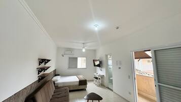 A bedroom with a bed, a sofa, a small table, a ceiling fan, and a window.