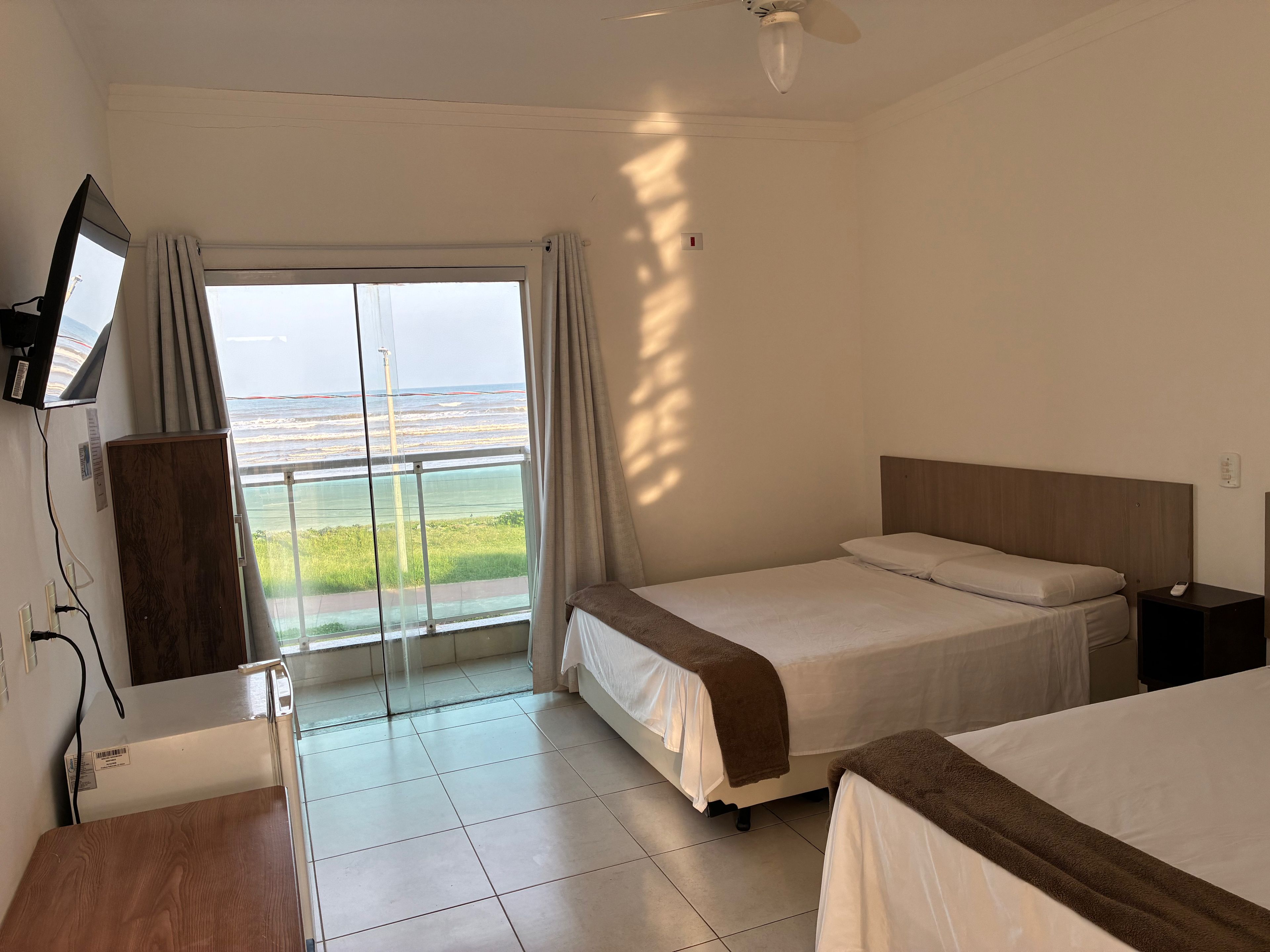A hotel room with a bed, a desk, a TV, and a view of the ocean.