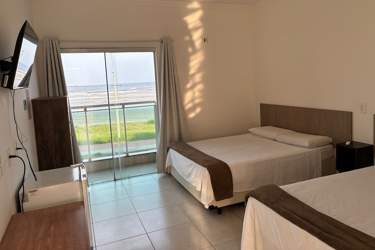 A hotel room with a bed, a desk, a TV, and a view of the ocean.