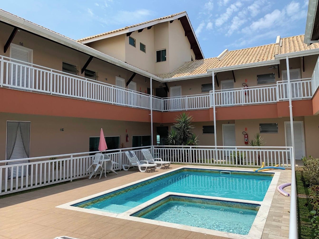 Un edificio de dos pisos con piscina, barandillas blancas y varios balcones.