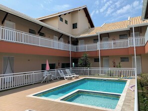 A two-story building with a swimming pool, white railings, and multiple balconies.