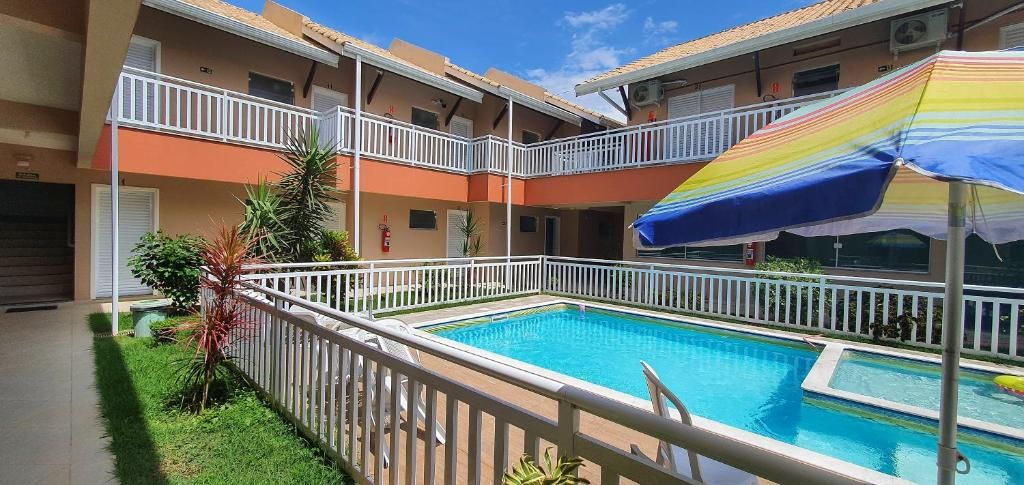 Un edificio de varios pisos con piscina, barandillas blancas y un paraguas de colores.