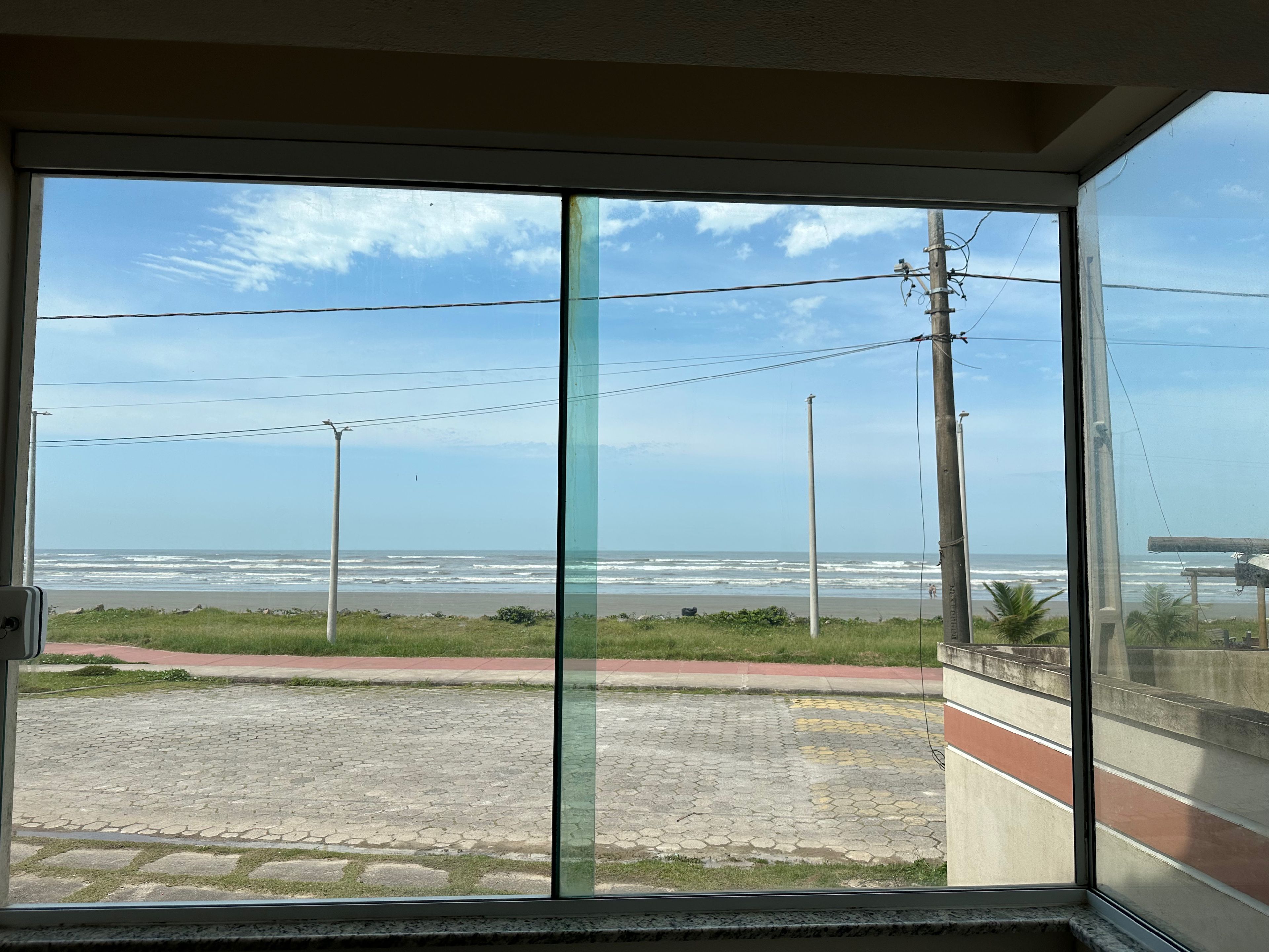 A view through a window with a paved area, a beach, and the ocean.