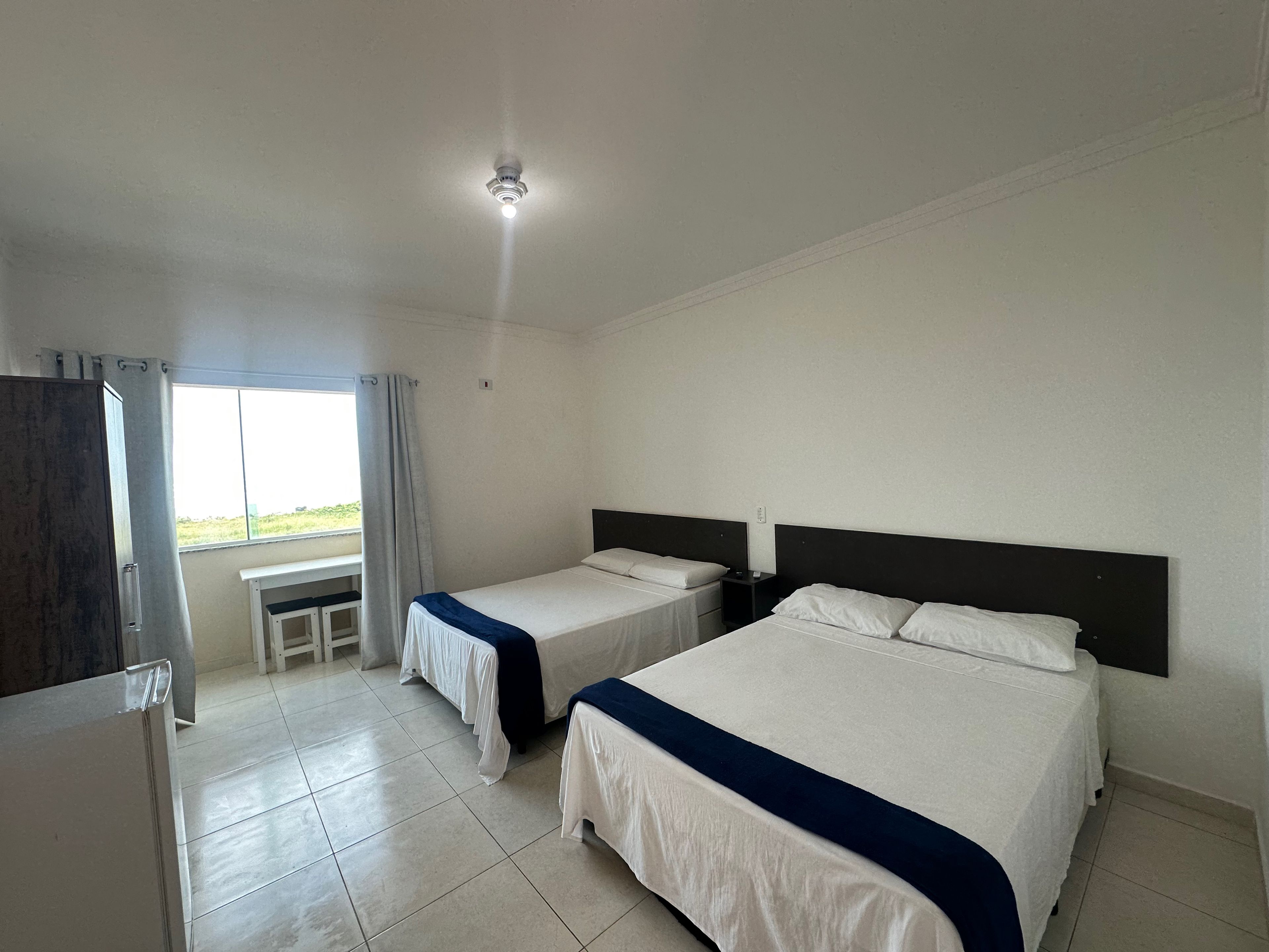 Een hotelkamer met twee eenpersoonsbedden, een bureau en een raam met gordijnen.