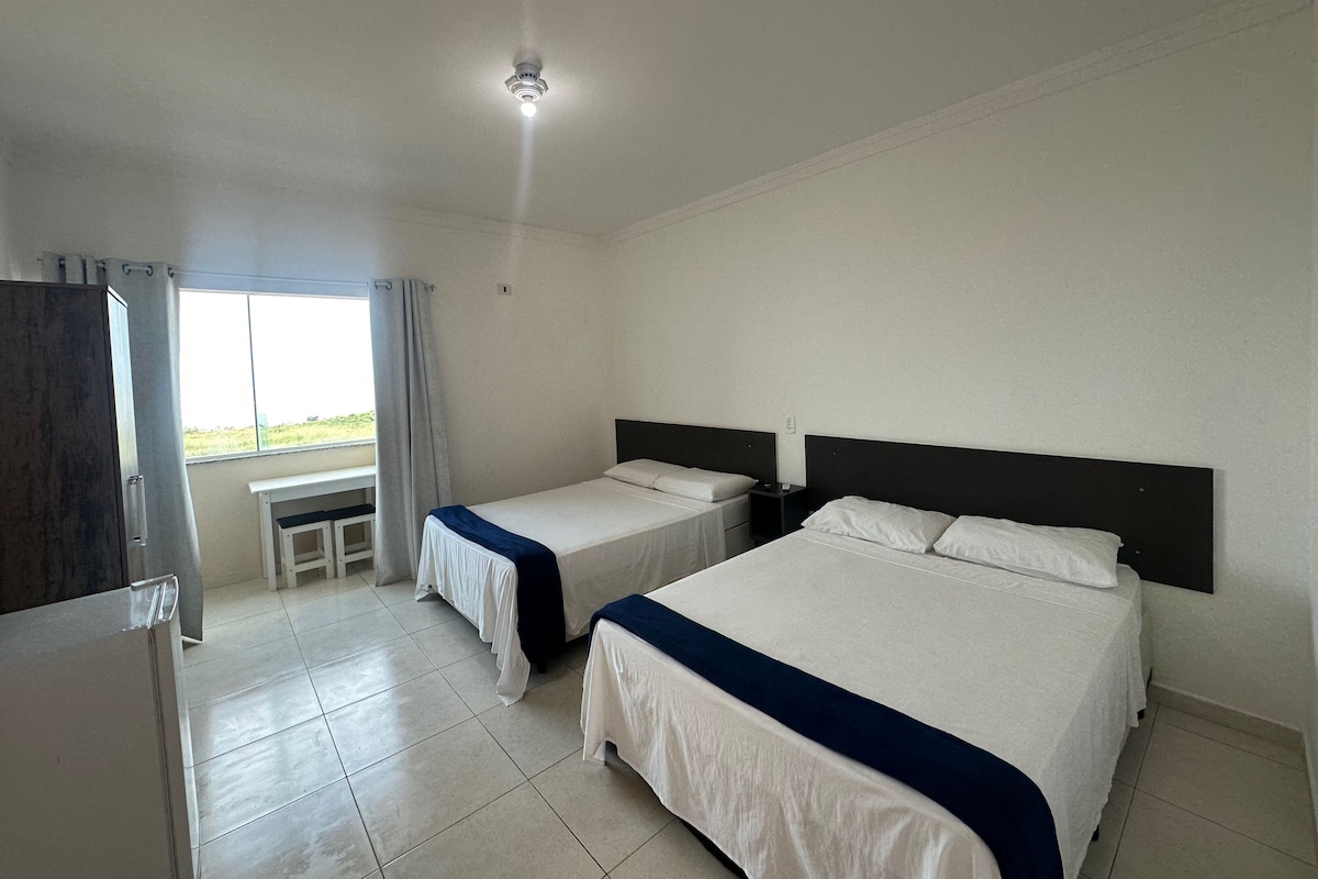 A hotel room with two single beds, a desk, and a window with curtains.