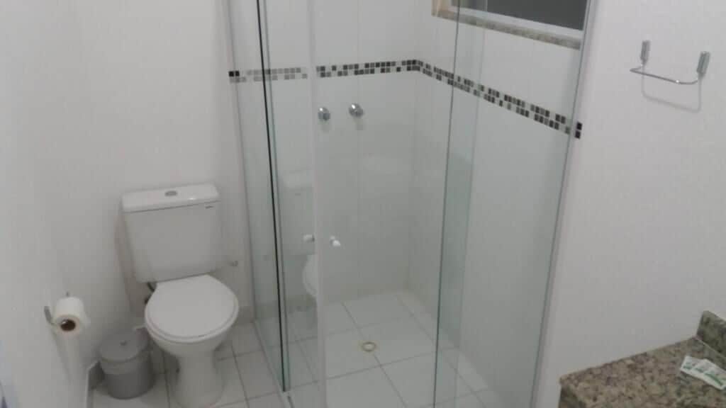 Un baño con inodoro, un cubo de basura y cabina de ducha con paredes de vidrio.