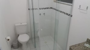 Casa de banho com sanita, um contentor de lixo e área de duche com parede de vidro.