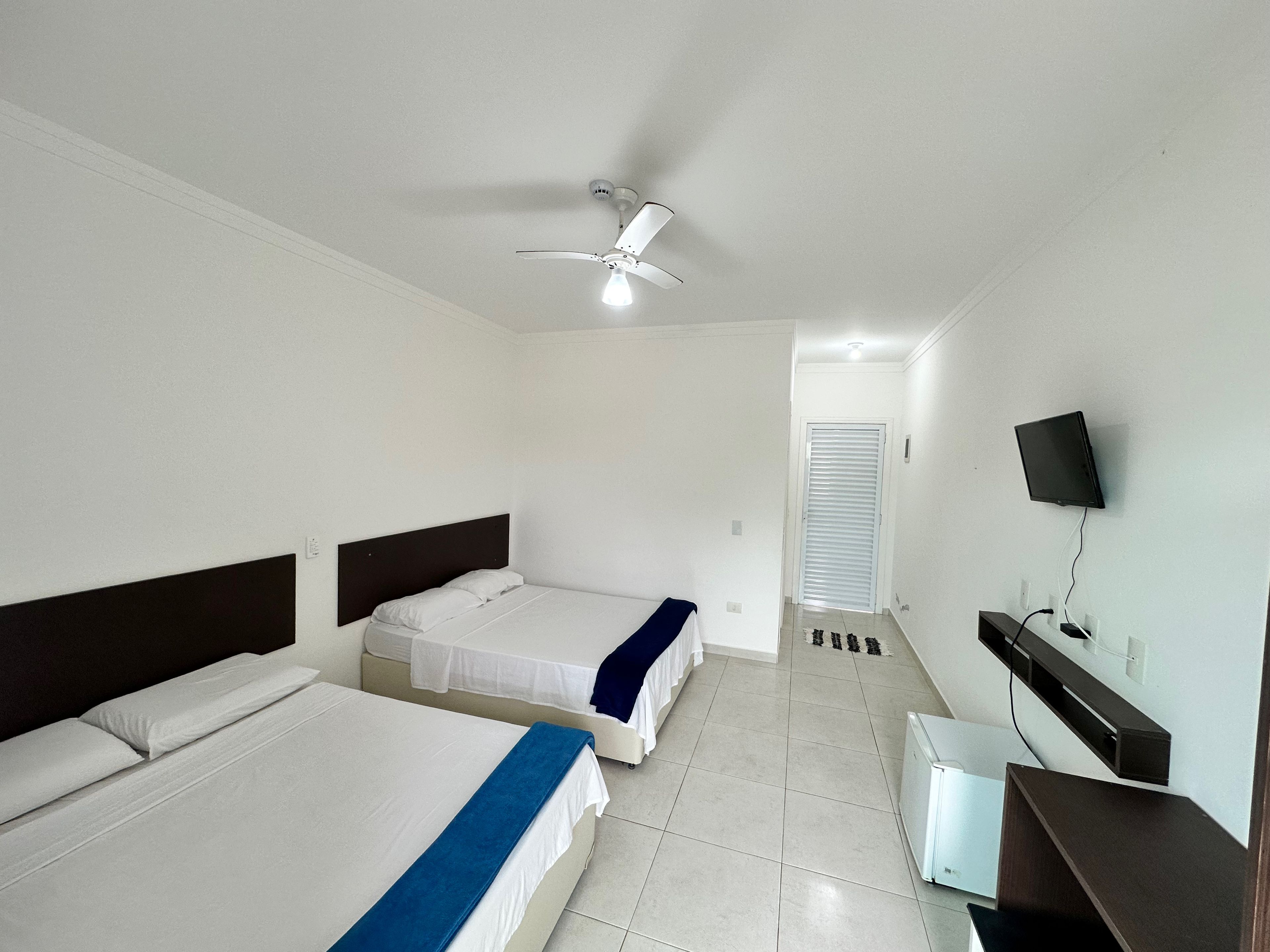 Habitación de hotel con dos camas, ventilador de techo, televisor montado en la pared y un escritorio pequeño.