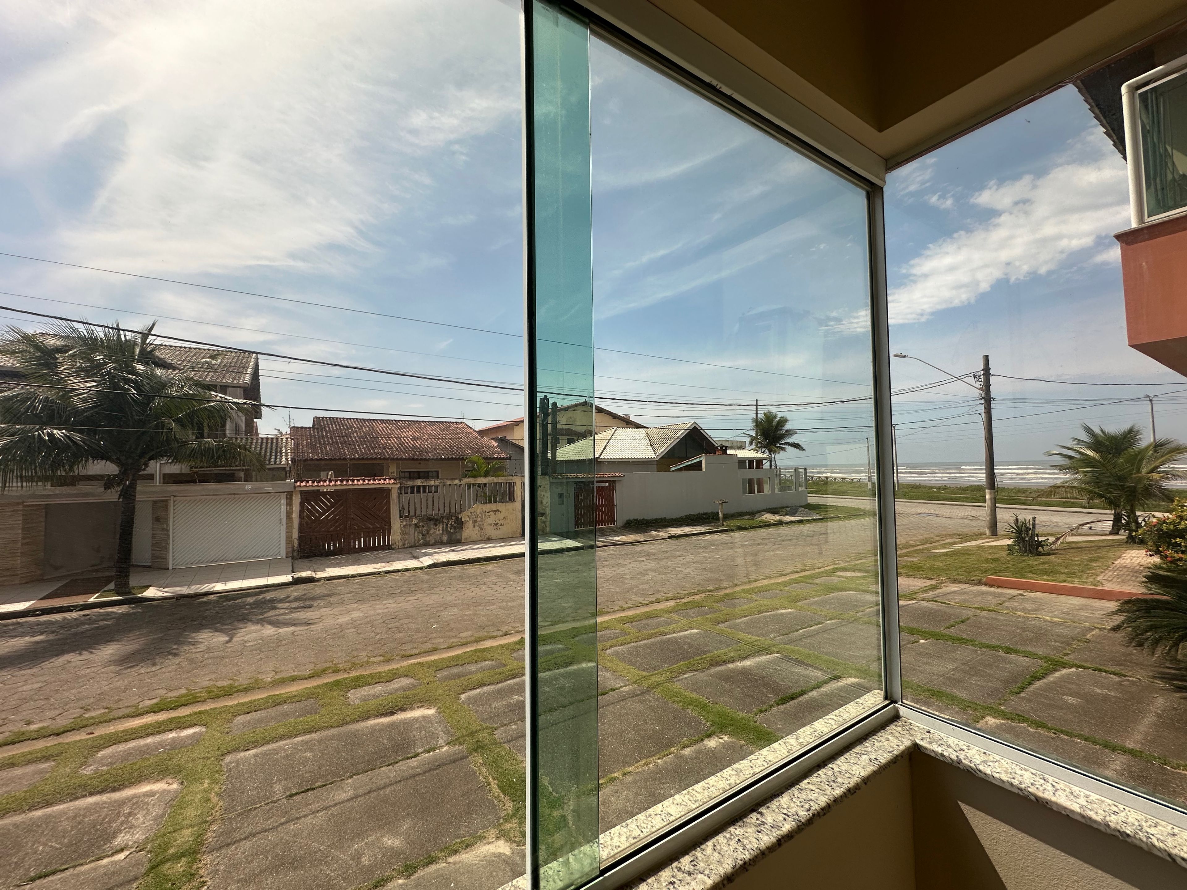 Rua residencial com casas, uma palmeira e céu claro.