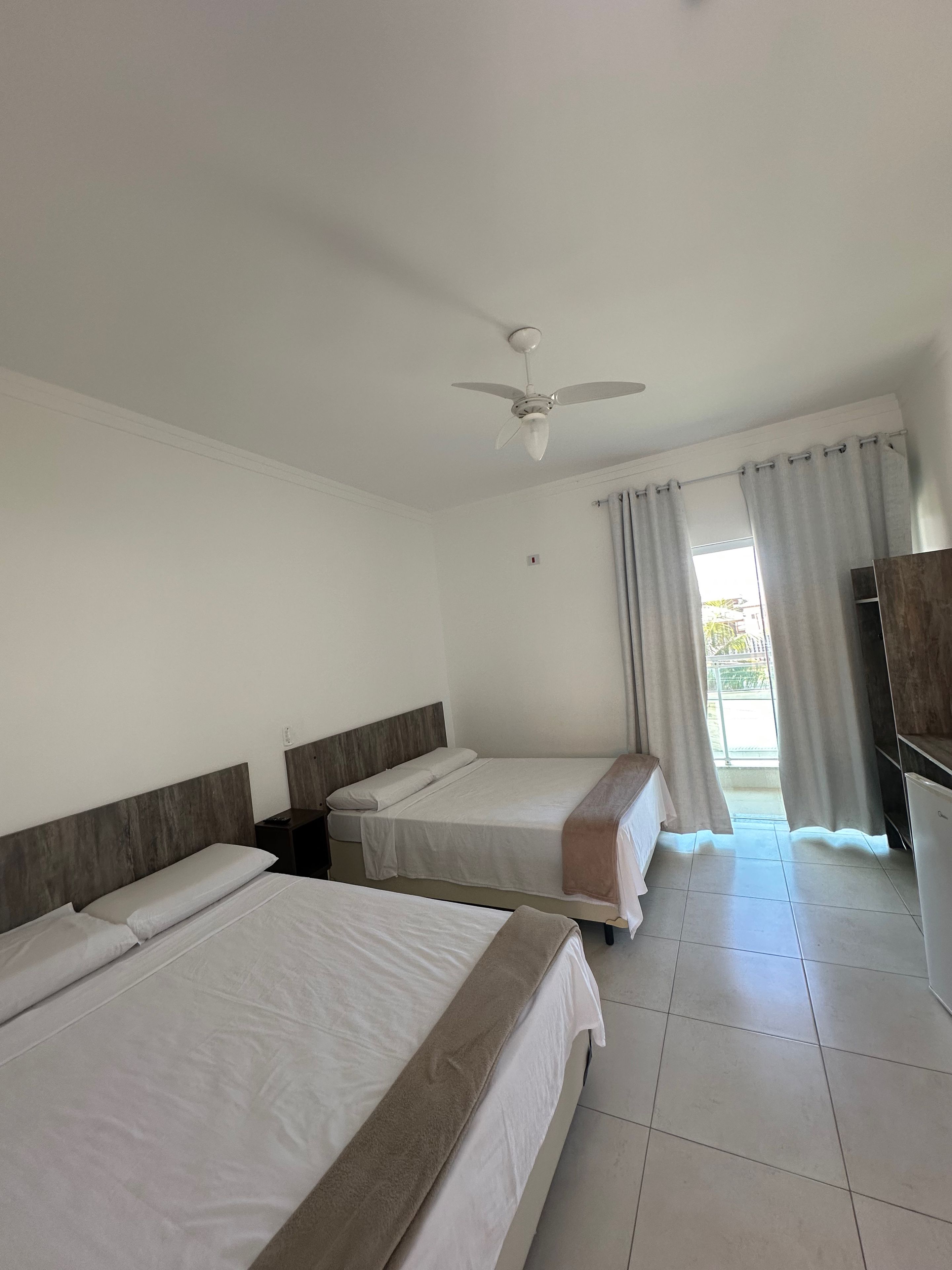 A hotel room with two beds, a ceiling fan, a window with curtains, and a TV.