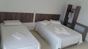 Quarto de hotel com duas camas individuais, cada uma com colcha e almofadas brancas, e cabeceira de madeira.