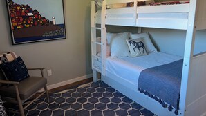 Un lit superposé avec un coussin en forme de cheval, un tableau encadré accroché au mur et un tapis à motifs hexagonaux.