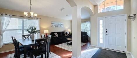 A spacious living area with a dining table, chairs, a sofa, and a chandelier.