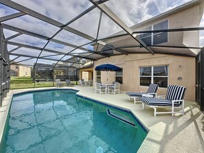 A swimming pool with a glass enclosure, lounge chairs, and a covered patio area. - Emerald Island Four Bed Pool Home close to Disney (Kissimmee)