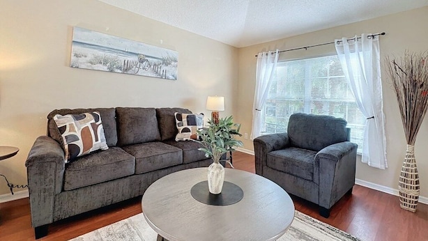 A living room with two grey sofas, a round coffee table, a painting on the wall, a window with curtains, and a vase with branches.