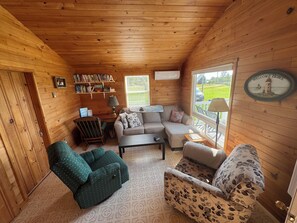 A cozy cabin interior with a sofa, armchairs, a bookshelf, and a window with a 'Welcome Home' sign. - Fogwell Oceanfront Retreat (Richmond)