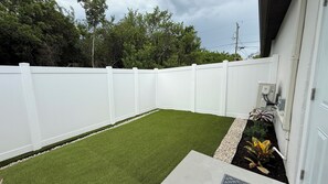 A fenced backyard with artificial grass and a small garden bed.