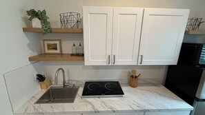 A kitchen with white cabinets, a black induction cooktop, a stainless steel sink, and a wooden countertop.