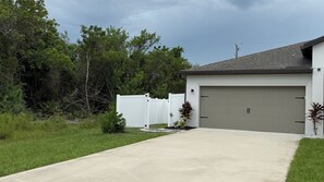 A residential driveway leading to a garage with a white fence and greenery around.