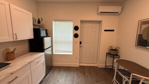 A compact kitchen with white cabinets, a refrigerator, a microwave, and a window with blinds.