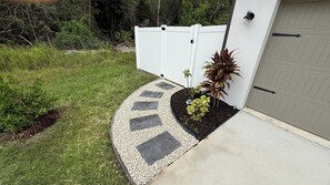 A residential driveway with a curved pathway leading to a garage, bordered by a white fence and a small garden with plants.