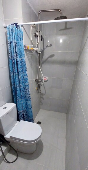 Cabine de banho pequena e fechada, com vaso sanitário, chuveiro e mangueira de banho.
