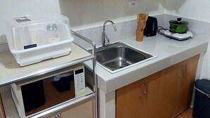 A compact kitchen with wooden cabinets, a stainless steel sink, a microwave, and a Megabox storage unit. - Cebu City Mabolo Resort Style (Cebu City)