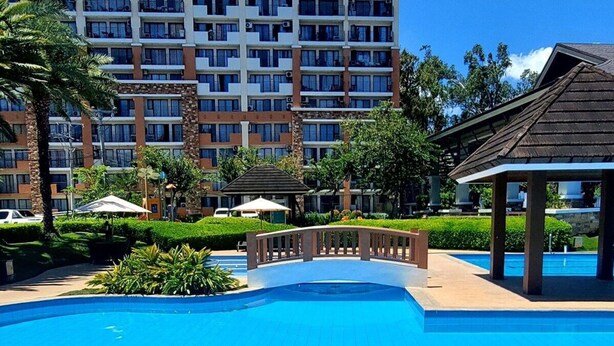 A swimming pool with a clear blue water surface, surrounded by a concrete deck. In the background, there is a multi-story building with balconies and a clear sky. - Cebu City Mabolo Resort Style (Cebu City)