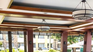 A spacious outdoor seating area with multiple sofas and tables, a wooden ceiling with a hanging light fixture, and a view of buildings and parked cars in the background. - Cebu City Mabolo Resort Style (Cebu City)