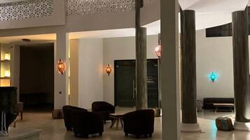 Un amplio vestíbulo con techos altos, una zona de estar con sofás y una mesa de centro, y una pared decorativa con diseños intrincados.