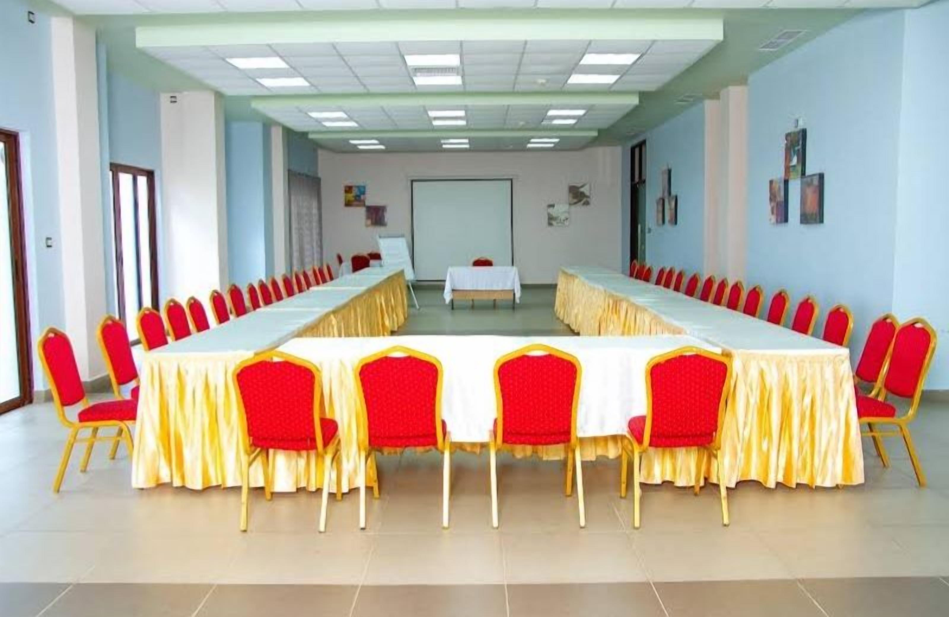 Un salón de conferencias con una larga mesa y sillas rojas, una pizarra y una pantalla de proyector.