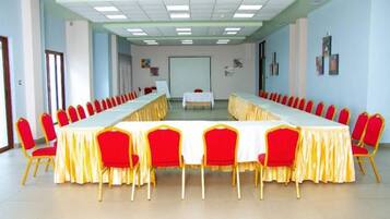 Un salón de conferencias con una larga mesa y sillas rojas, una pizarra y una pantalla de proyector.