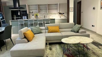 Una sala moderna con un sofá modular, una mesa de comedor y una cocina al fondo.