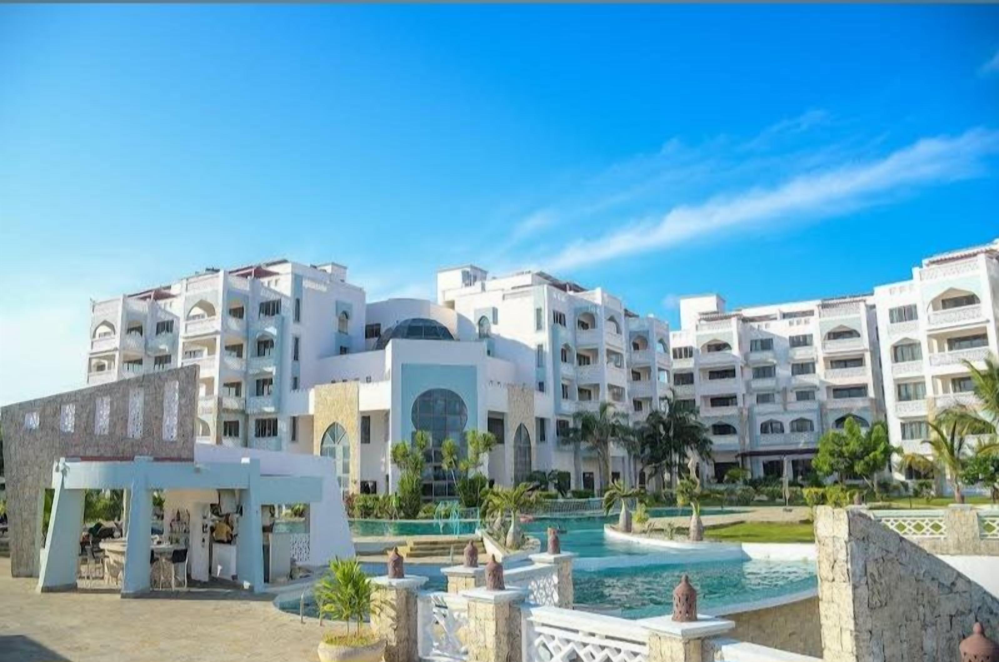 A hotel with multiple floors, a swimming pool, and a landscaped area with palm trees.