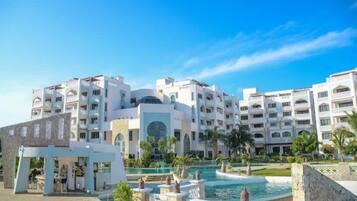 A hotel with multiple floors, a swimming pool, and a landscaped area with palm trees.