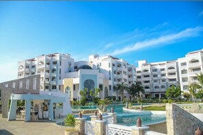 Un hotel con varios pisos, piscina y un área ajardinada con palmeras.
