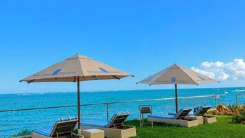 Un espace aménagé au bord de la piscine, avec des chaises longues et des parasols, offrant une vue sur un océan d’un bleu limpide.