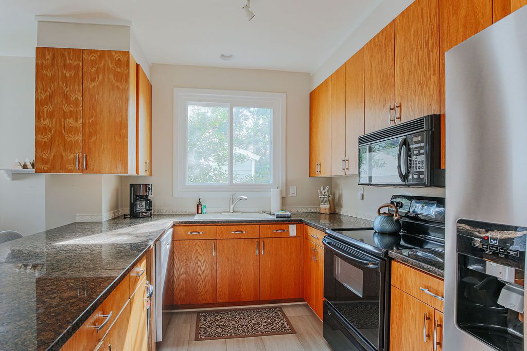 A kitchen with wooden cabinets, a stainless steel refrigerator, a microwave, and a stove.