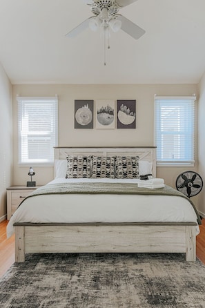 Une chambre à coucher avec un lit, un ventilateur de plafond, une table de chevet avec une lampe et des œuvres d’art accrochées au mur.