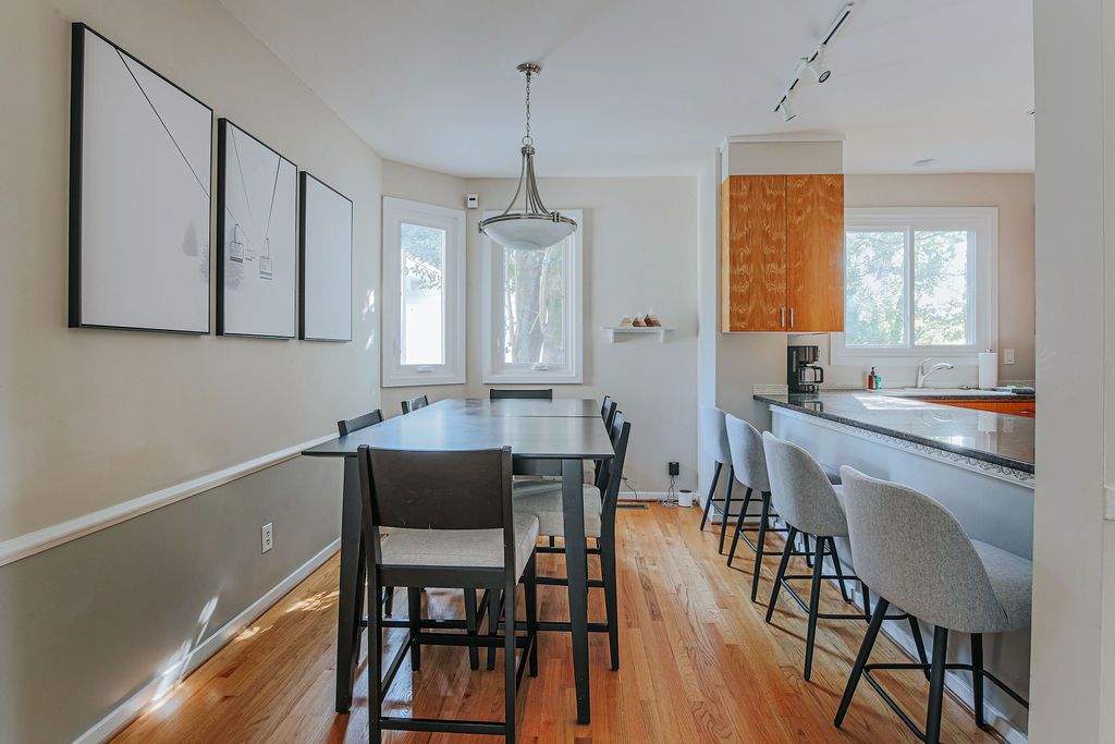 A modern kitchen with a dining area, wooden flooring, and a pendant light.